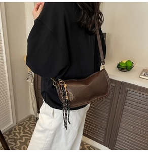 Detailed view of dark brown leather crossbody bag featuring tennis racket charm and tassels