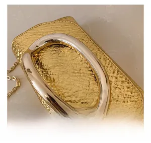 Detail of snake-embossed gold leather texture and U-shaped metal handle on luxury evening bag