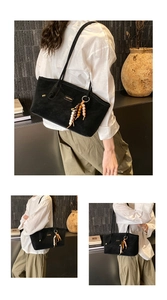 Detail of black suede tote bag featuring a metal logo and wooden bead charm accessory