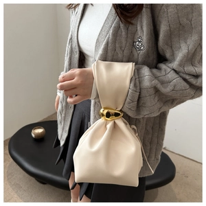 Close-up of cream drawstring bucket bag featuring a unique oval gold metal buckle detail