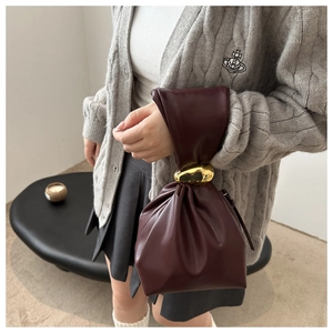 Close-up of deep wine red pleated bucket bag featuring unique irregular gold metal handle