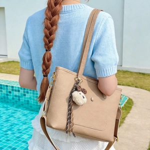 Brown leather tote bag with pompom pendant shown in a stylish outdoor setting