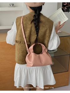 Sac dumpling en cuir souple rose pâle porté à l'épaule dans un décor minimaliste