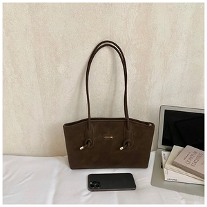 Detailed close-up of dark brown suede tote bag with metal nameplate and knotted handle