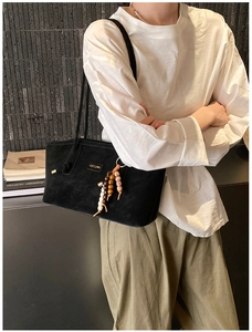 Detail of black suede tote bag featuring a metallic logo and stylish beaded tassel charm