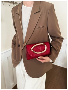 Detail of red patent leather handbag with gold chain strap and oval metal clasp closure