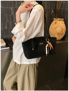 Detail of a large black suede tote bag featuring ethnic wooden bead tassels and metal logo