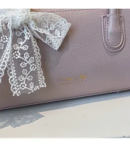 Détail d'un sac en cuir mauve avec un grand nœud en dentelle blanche et logo doré