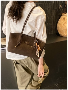 Detail of dark brown suede tote bag with a colorful beaded charm and brand logo