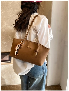 Brown leather tote bag shown on shoulder with stylish wooden beaded charm detail