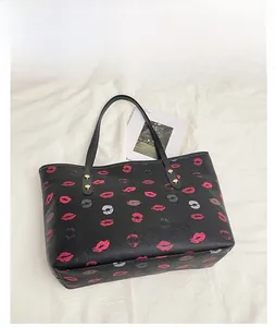 Close-up of black leather tote bag featuring vibrant red lip prints and gold stud accents