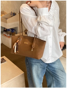 Close-up of brown tote bag featuring wood and white bead tassel with brand logo detail