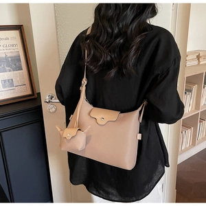 Detail of beige shoulder bag with a mini coin purse charm worn by a model in a room