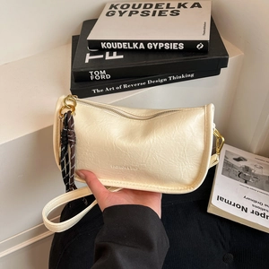 Chic cream litchi-textured half-moon tote bag with woven tassel on stylish magazines