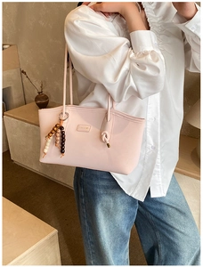Close-up of pink tote bag featuring a wooden bead tassel charm and brand logo plate