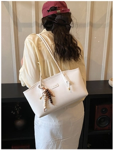 Close-up of a white leather tote bag featuring a beaded tassel and brand leather label