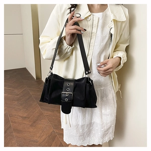 On-body view of a black pleated square shoulder bag with wide buckled leather strap
