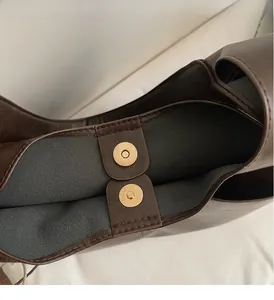 Detail of a gold magnetic snap closure on a premium dark brown leather tote handbag
