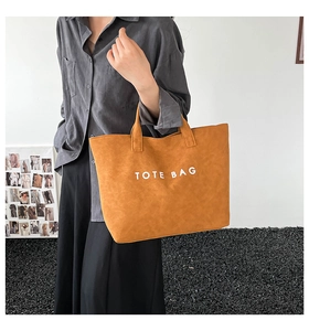 Detailed view of a mustard yellow large tote bag with TOTE BAG print worn by a model