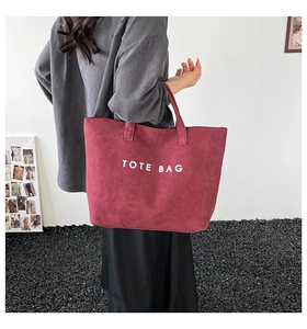 Model wearing a large burgundy tote bag made of matte suede with white printed letters