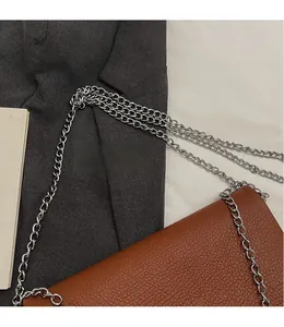 Détail d'un sac enveloppe en cuir grainé marron avec bandoulière en chaîne de métal argenté