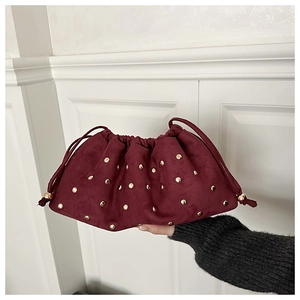 Gros plan d'une pochette froncée bordeaux en daim avec rivets dorés et cordon de serrage