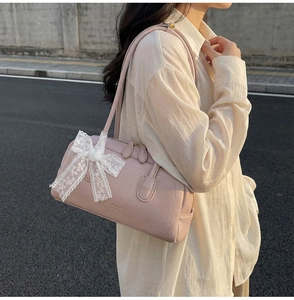 Detail of light pink Boston bag featuring a white lace bow charm and lychee leather texture