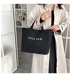 Side view of a black suede tote bag with white lettering worn by a model in a beige coat