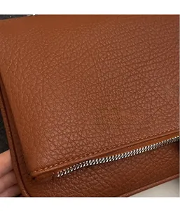 Gros plan sur la texture du cuir litchi marron et la fermeture éclair argentée du sac