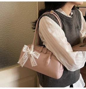 Detail of light pink Boston bag featuring a white lace bow and pebbled leather texture