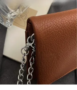 Détail macro du fermoir mousqueton argenté sur sac en cuir marron à grain de litchi