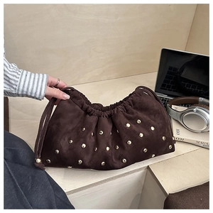 Détail du sac seau en cuir mat marron foncé avec rivets dorés dans un cadre décontracté