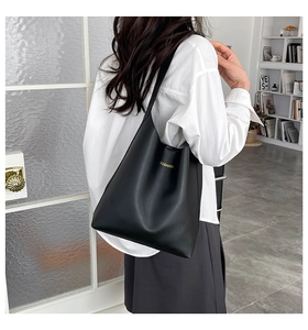 Rear view of a model wearing a large black minimalist tote bag with gold logo lettering