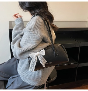 Detailed view of the side-mounted white lace bow on the black leather Boston bag