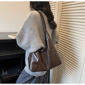 Detail of deep brown PU leather tote bag with wide strap on shoulder shown by model