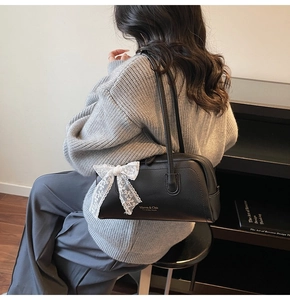 Detailed close-up of a black lychee leather Boston bag with a delicate white lace bow accent