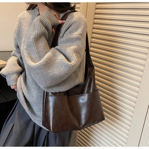 Detail of a large dark brown faux leather tote bag with wide shoulder strap and front pockets
