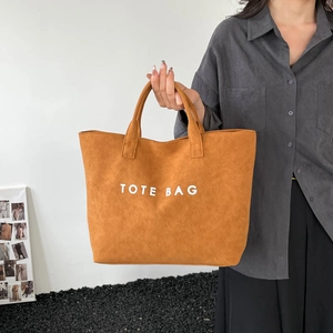 Minimalist tan tote bag in brushed suede leather texture with bold TOTE BAG lettering