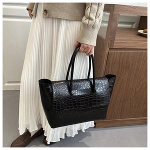 Close-up of black crocodile pattern tote bag held by model for vintage office style