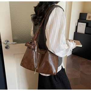 Detail of dark brown tote bag featuring soft leather texture and white woven tassel charm
