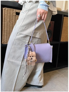 Detail view of purple leather handbag with metal studs and a cute brown puppy plush charm