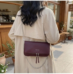 Detail of burgundy lychee grain leather crossbody bag with silver chain and tassels