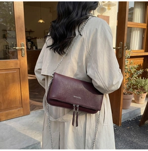 Detail of burgundy lychee grain leather crossbody bag with silver chain and tassels