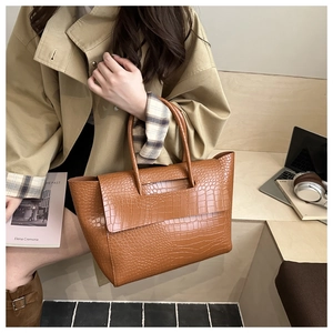 Close-up of brown crocodile pattern tote bag held by model in a minimalist home setting
