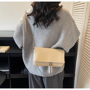 Sac bandoulière beige en cuir grainé avec chaîne argentée porté par un mannequin