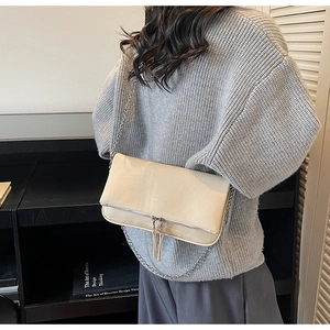 Détail d'un sac baguette blanc crème avec chaîne argentée et pompons sur un tricot doux