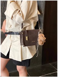 Detail of dark brown matte leather box bag with gold buckle and plush bear pendant