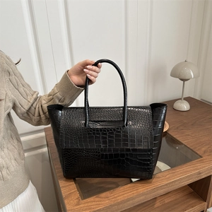 Detail of black crocodile texture tote bag shown on model with cozy knit sweater