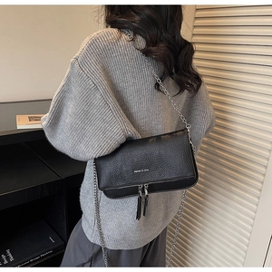 Detail of black litchi grain leather crossbody bag with silver chain and dual zippers