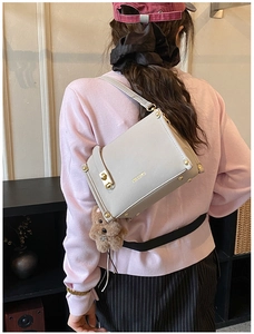 Detail of light gray crossbody bag with gold hardware and plush bear charm on model